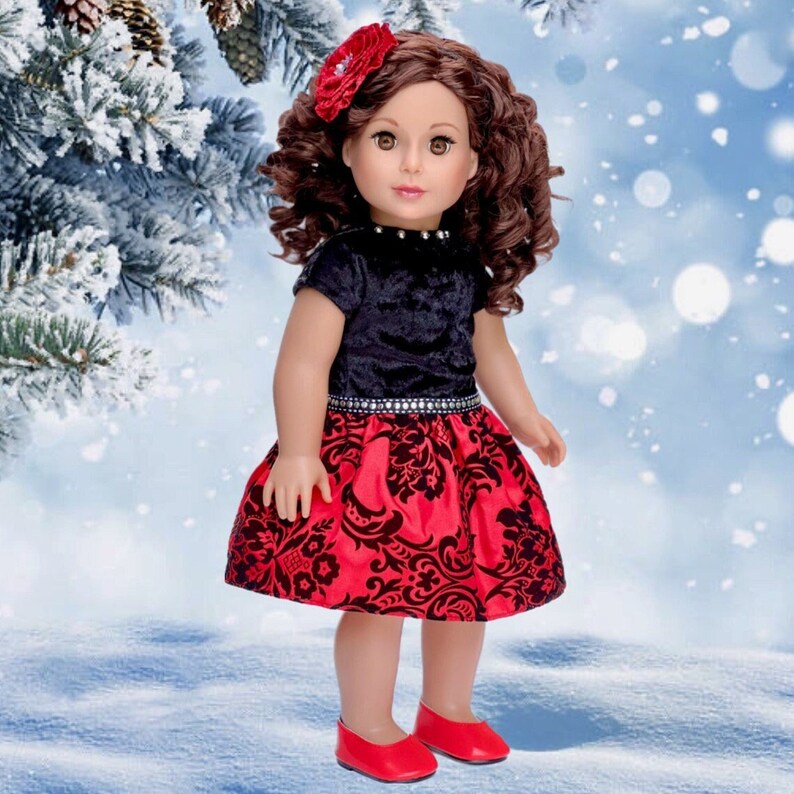 May include: A doll with brown curly hair and a red flower hair accessory. The doll wears a black velvet short-sleeved top with a silver-studded neckline and a red skirt featuring a black floral pattern and a silver-studded waist. Red shoes.