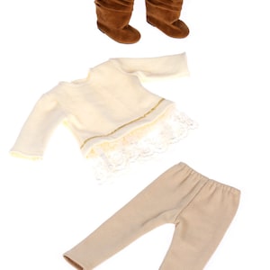 May include: A three-piece outfit for a doll, including a cream-colored sweater with lace trim, beige leggings, and brown suede boots.