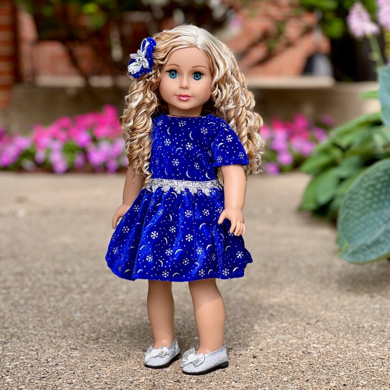 K&ouml;nnte beinhalten: Eine Puppe tr&auml;gt ein blaues Samtkleid mit silbernen Schneeflocken und Monden. Das Kleid hat einen silbernen G&uuml;rtel und die Puppe hat blonde lockige Haare und blaue Augen.
