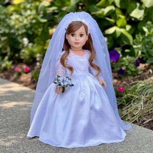 May include: A white satin bridal gown with lace detailing and a long tulle veil. The doll is holding a small bouquet of white flowers.