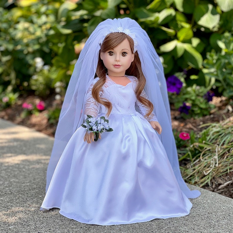 May include: A white satin bridal gown with lace detailing and a long tulle veil. The doll is holding a small bouquet of white flowers.