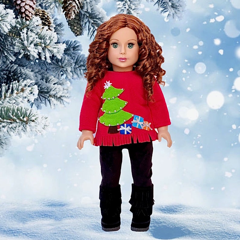 May include: A red Christmas sweater with a green felt Christmas tree and presents on the front. The sweater has a fringe trim and is worn by a doll with long curly red hair.
