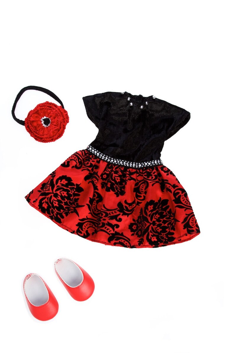 May include: A black and red dress with a short-sleeved black bodice, a red skirt featuring a black damask pattern, and a silver-toned beaded waistband. Included are a red fabric flower headband and a pair of solid red slip-on shoes.