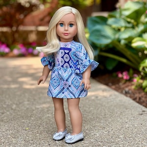 May include: A doll with long blonde hair wearing a blue and white patterned dress with ruffled sleeves and silver shoes.