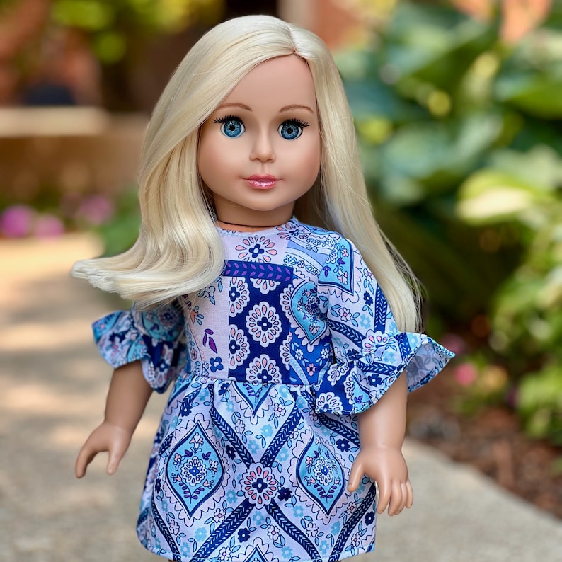 May include: A doll with long blonde hair wearing a blue and white patterned dress with ruffled sleeves.