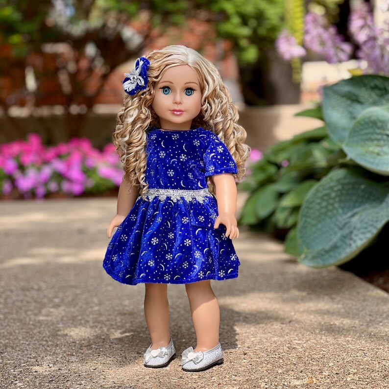 K&ouml;nnte beinhalten: Eine Puppe tr&auml;gt ein blaues Samtkleid mit silbernen Schneeflocken und Monden. Das Kleid hat einen silbernen Glitzerr&uuml;cken. Die Puppe hat blonde lockige Haare und tr&auml;gt silberne Schuhe.