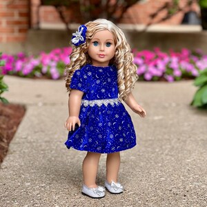 K&ouml;nnte beinhalten: Eine Puppe tr&auml;gt ein blaues Samtkleid mit silbernen Schneeflocken und Monden. Das Kleid hat einen silbernen Glitzerr&uuml;cken und die Puppe hat blonde lockige Haare und blaue Augen.