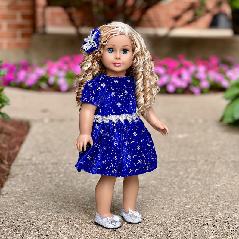 K&ouml;nnte beinhalten: Eine Puppe tr&auml;gt ein blaues Samtkleid mit silbernen Schneeflocken und Monden. Das Kleid hat einen silbernen Glitzerr&uuml;cken und die Puppe hat blonde lockige Haare und blaue Augen.