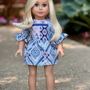 May include: A blonde doll wearing a blue and white patterned dress with ruffled sleeves and silver shoes.
