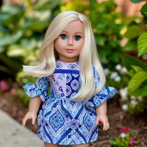 May include: A doll with long blonde hair wearing a blue and white patterned dress with pink accents.