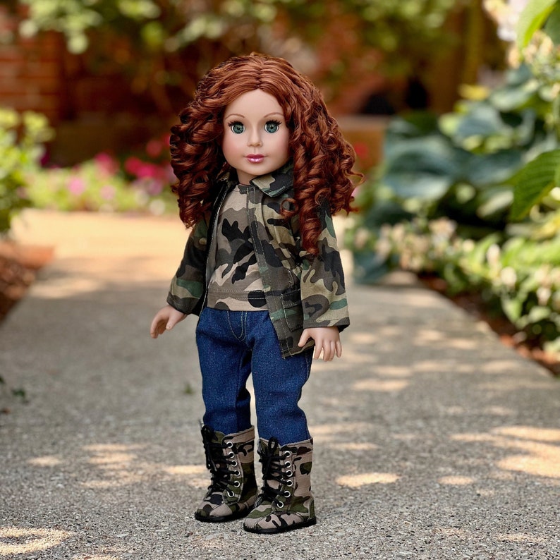 May include: A doll with long curly auburn hair and green eyes wearing a camouflage print jacket over a matching camouflage t-shirt, dark blue denim jeans, and camouflage print lace-up boots with silver eyelets and black laces.