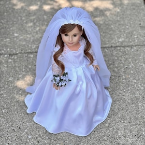 May include: A white bridal gown with a lace bodice and a tulle veil. The doll is holding a small bouquet of white flowers.