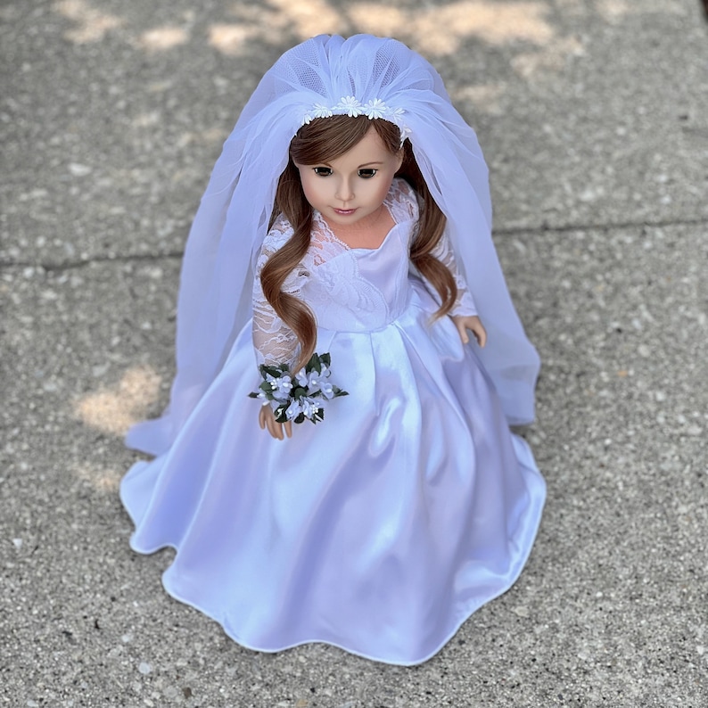 May include: A white bridal gown with a lace bodice and a tulle veil. The doll is holding a small bouquet of white flowers.