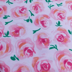 May include: Close-up of a fabric with a repeating pattern of watercolor roses. The roses are in shades of pink and orange, with green leaves on a white background. The design is soft and floral.