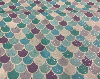 May include: Fabric with a mermaid scale pattern in shades of blue, teal, purple, and white. The scales have a slight shimmer, and the fabric is likely used for crafting or apparel.