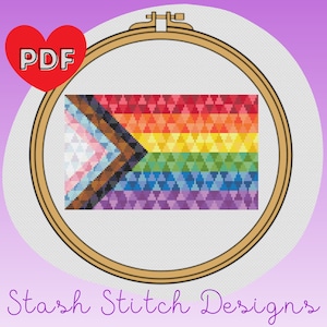 Op de afbeelding: Een PDF-patroon voor een kruissteekontwerp van een regenboogvlag met een transgender pride chevron. De vlag bevindt zich in een houten borduurring.