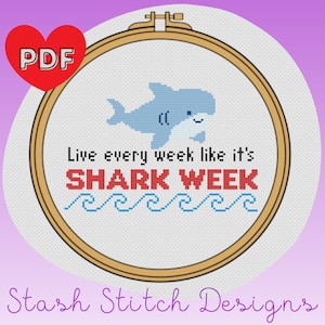 Puede incluir: Un patrón de punto de cruz con un tiburón de dibujos animados con el texto "Live every week like it's Shark Week". El patrón se muestra en un aro de bordado de madera.