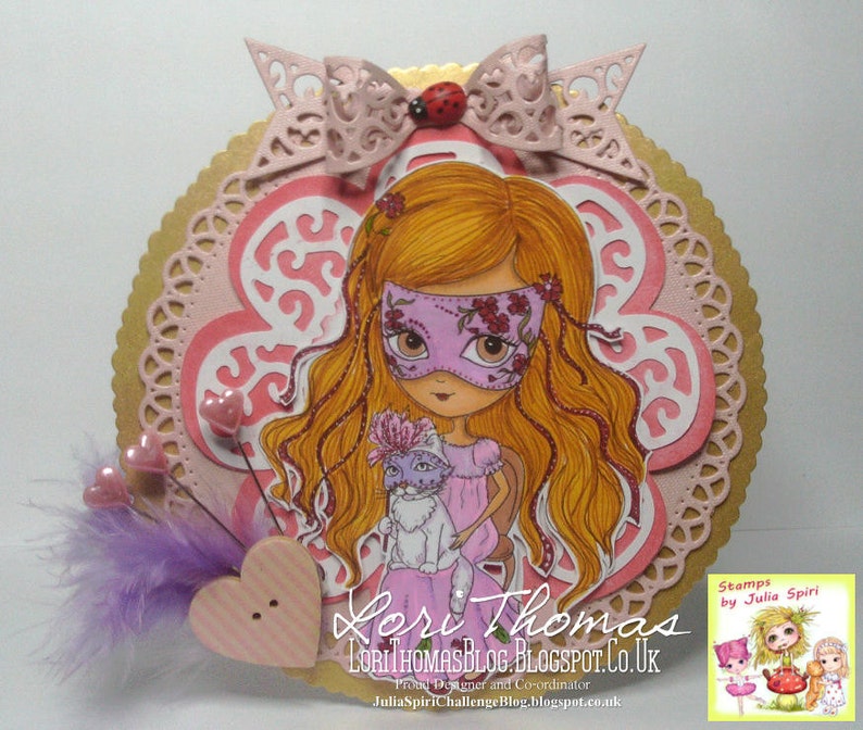 May include: A pink and gold card with a girl wearing a pink mask and holding a white cat. The card has a pink and white flower design and the text "Lori Thomas LoriThomasBlog.Blogspot.co.uk Proud Designer and Co-ordinator JuliaSpiriChallengeBlog.blogspot.co.uk Stamps by Julia Spiri" is printed on the card.