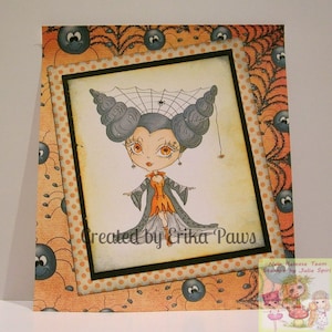 May include: A Halloween-themed card featuring a cartoon illustration of a girl with spiderweb hair and a black dress. The card has a polka dot background and a border of spiders and spiderwebs. The text "Created by Erika Paws" is printed on the card.