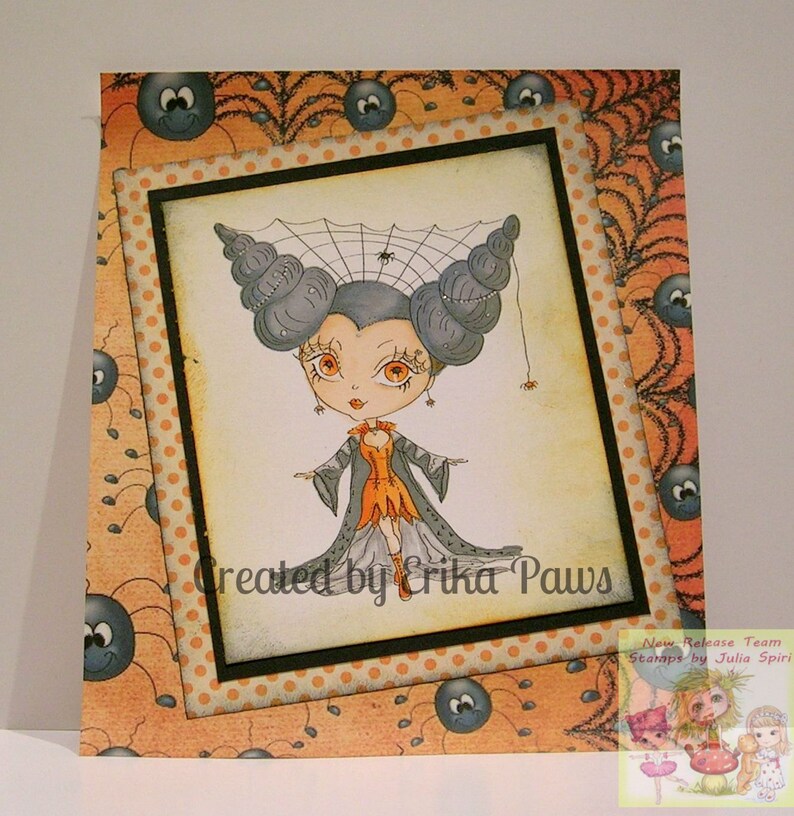 May include: A Halloween-themed card featuring a cartoon illustration of a girl with spiderweb hair and a black dress. The card has a polka dot background and a border of spiders and spiderwebs. The text "Created by Erika Paws" is printed on the card.
