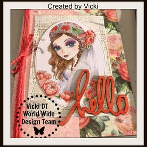 May include: A handmade card with a floral design featuring a woman with long brown hair wearing a floral headband and a veil. The card has a wooden cutout of the word "hello" in orange. The card also has a black and white butterfly graphic and the text "Vicki DT World Wide Design Team".