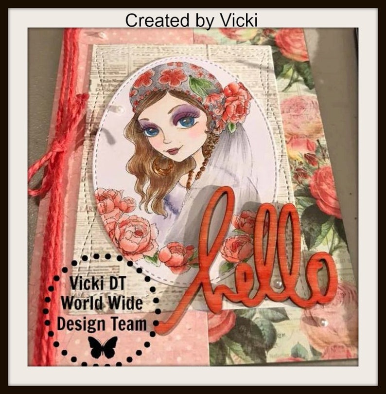 May include: A handmade card with a floral design featuring a woman with long brown hair wearing a floral headband and a veil. The card has a wooden cutout of the word "hello" in orange. The card also has a black and white butterfly graphic and the text "Vicki DT World Wide Design Team".