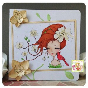 May include: A handmade greeting card featuring a whimsical illustration of a woman with red hair and a cardinal bird. The woman is surrounded by white flowers and green leaves. The card has a white background and a wooden frame.