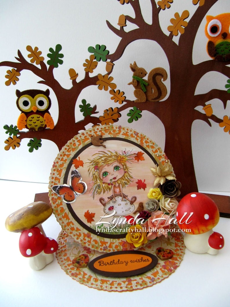 May include: A handmade autumn-themed birthday card with a layered design. The card features a whimsical girl with a butterfly, a squirrel, owls, and mushrooms. The card is decorated with fall leaves, flowers, and a brown banner with the text "Birthday wishes".