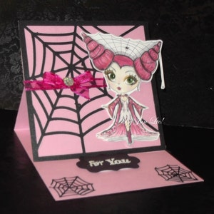 May include: A pink and black Halloween card with a spiderweb design. The card features a cartoon illustration of a girl with pink hair and a spiderweb crown. The card says "For You" on the front.