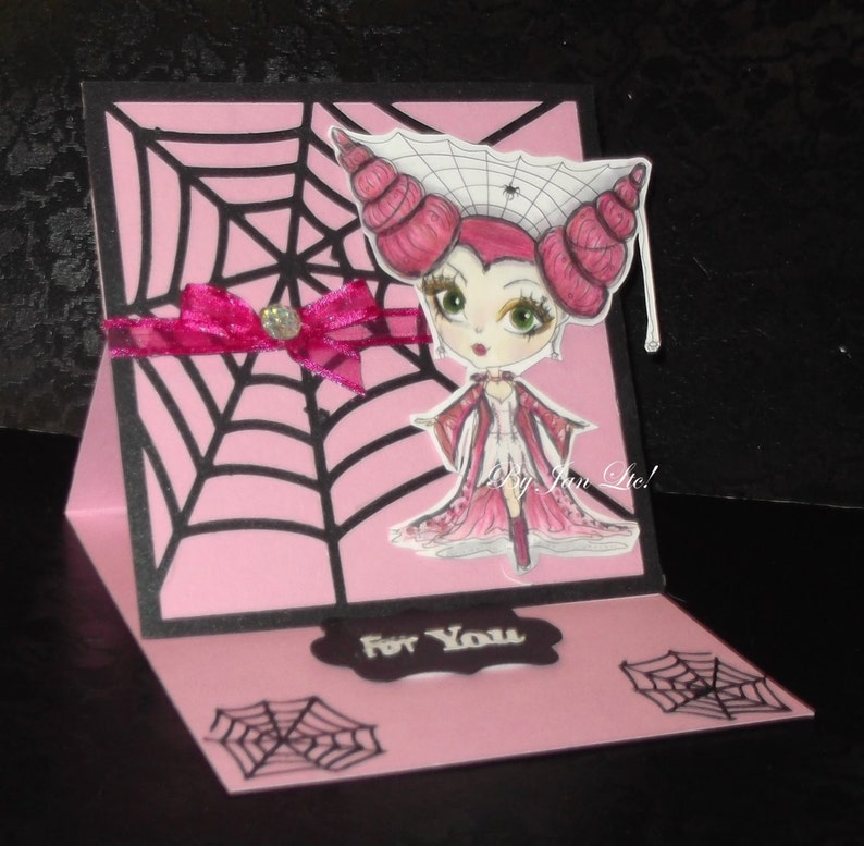 May include: A pink and black Halloween card with a spiderweb design. The card features a cartoon illustration of a girl with pink hair and a spiderweb crown. The card says "For You" on the front.