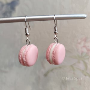 Könnte beinhalten: Ein Paar Ohrringe in Form von rosa und weißen Macarons mit silbernen Haken. Die Macarons sind aus Polymer Clay gefertigt und haben ein realistisches Aussehen.