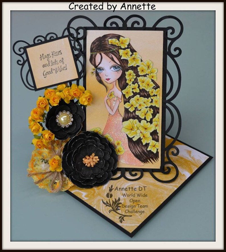 May include: A handmade card with a black frame and a yellow background. The card features a cartoon girl with long brown hair and a yellow flower crown. The card also includes a black and yellow flower embellishment and a sign that says "Hugs, Kisses and lots of Good Wishes!"
