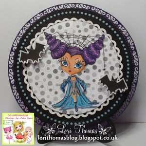May include: A purple and blue witch with a spider web on her head, wearing a blue dress and holding a wand. She is surrounded by bats and a polka dot background. The image is framed with a black and purple border.
