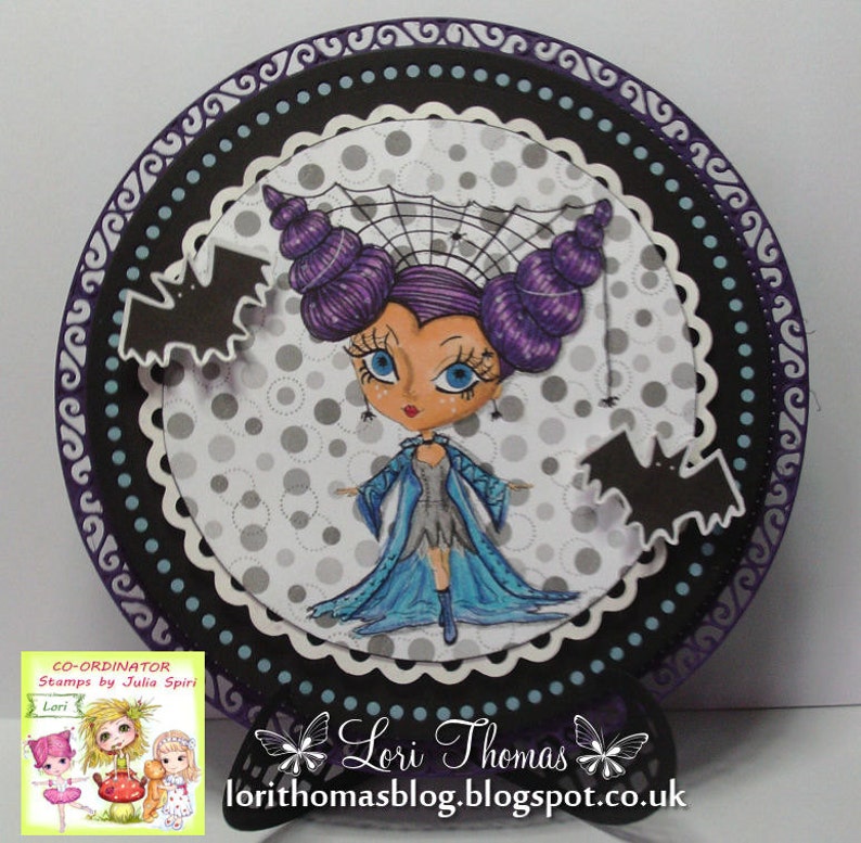 May include: A purple and blue witch with a spider web on her head, wearing a blue dress and holding a wand. She is surrounded by bats and a polka dot background. The image is framed with a black and purple border.