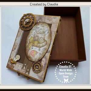 May include: A brown wooden box with a decorative lid featuring a whimsical illustration of a mouse wearing a hat with gears and clocks. The box is decorated with gold accents and a vintage newspaper print. The text "Created by Claudia" is visible on the lid. The box is open and empty.