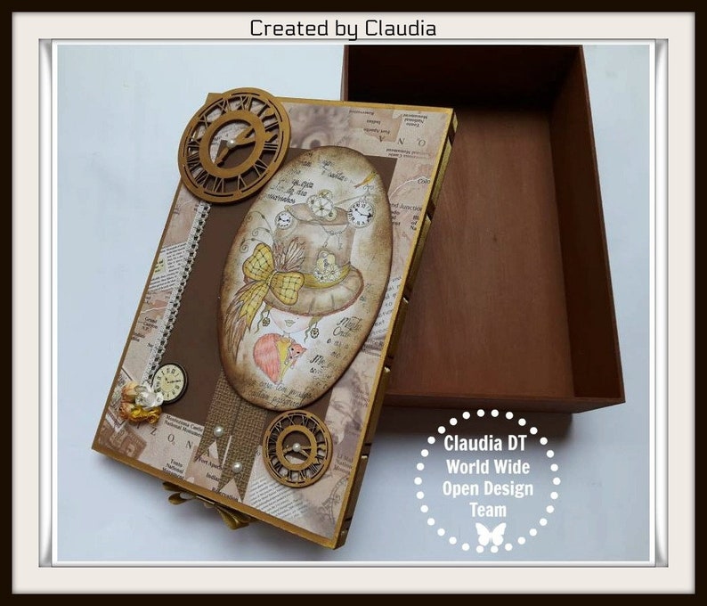 May include: A brown wooden box with a decorative lid featuring a whimsical illustration of a mouse wearing a hat with gears and clocks. The box is decorated with gold accents and a vintage newspaper print. The text "Created by Claudia" is visible on the lid. The box is open and empty.