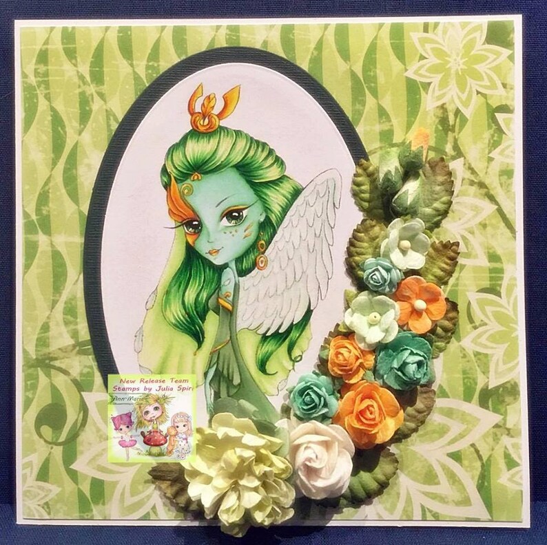May include: A green and white fairy with wings and a crown, surrounded by flowers and leaves. The image includes the text "New Release Team Stamps by Julia Spiry".