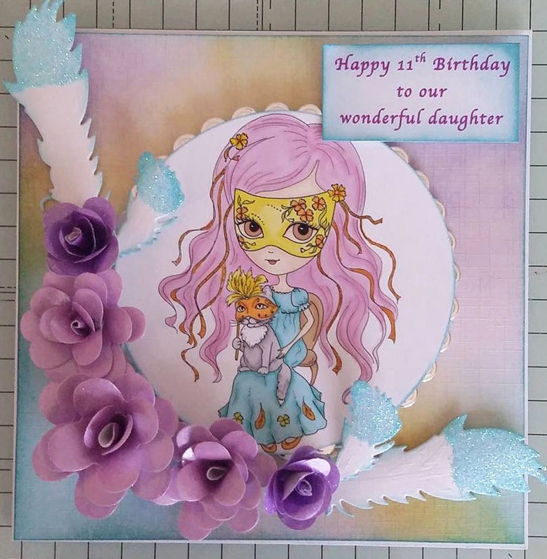 May include: A handmade card with a purple, pink, and blue color scheme. The card features a girl with pink hair wearing a yellow mask and holding a cat. The card has the text "Happy 11th Birthday to our wonderful daughter".
