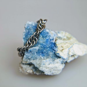 May include: A silver chain necklace resting on a blue and white crystal rock.