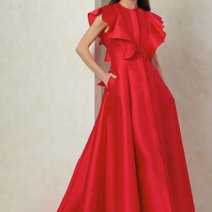 Puede incluir: Un vestido rojo de largo hasta el suelo con un escote y mangas con volantes. El vestido tiene un corpi&ntilde;o ajustado y una falda fluida con cola.
