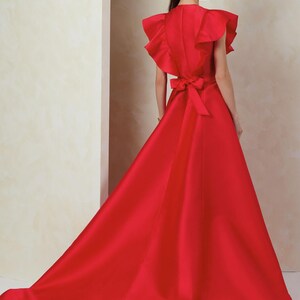 Puede incluir: Un vestido de sat&eacute;n rojo con un escote de volantes y un lazo en la cintura.