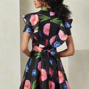 Puede incluir: Un vestido negro con estampado floral con flores rosas, azules y verdes. El vestido tiene un cuello y mangas con volantes, y un lazo en la espalda.