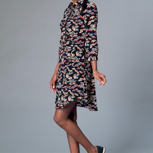 May include: A black dress with a cloud pattern in red, white, and blue. The dress has a collared neckline, long sleeves, and a slightly flared skirt. The model is wearing black loafers.