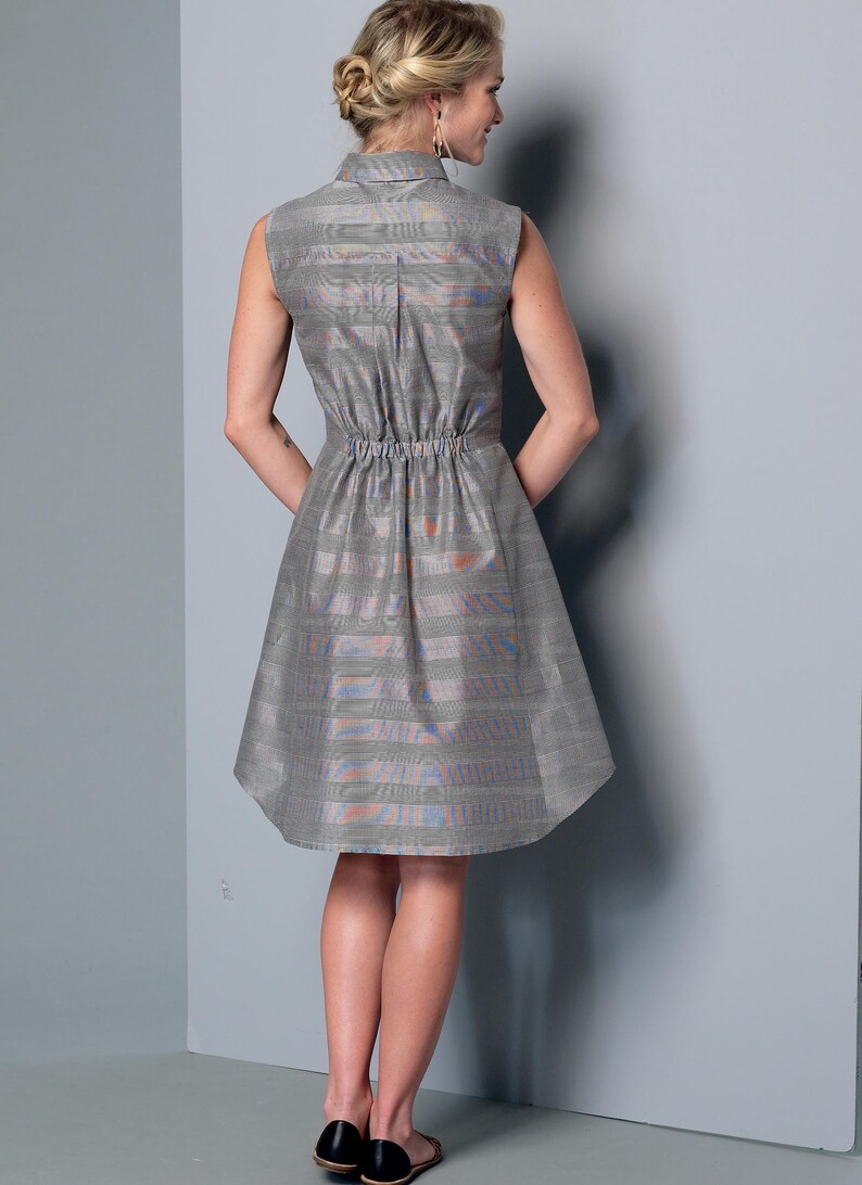 May include: Sleeveless gray dress with a collared neckline and elastic waist. The dress features a subtle striped pattern with hints of orange and blue. The skirt flares out from the waist. The model is wearing black flats.