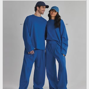 May include: Simplicity S3281 sewing pattern envelope featuring a blue long-sleeve crewneck top and matching wide-leg trousers. The design includes baseball caps and is labeled with A,C and B,C. The text reads Simplicity and Designed and printed in USA.
