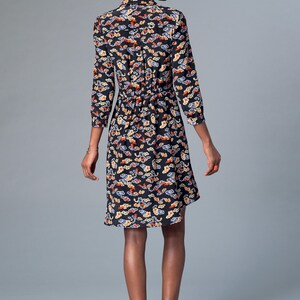 May include: Black dress with a colorful cloud pattern. The dress has a collared neckline, three-quarter sleeves, and a cinched waist. The hemline falls to the knees. The model is wearing black flats.