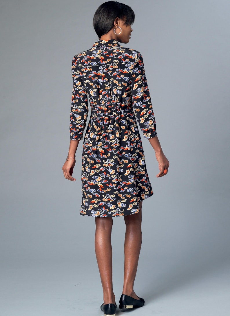 May include: Black dress with a colorful cloud pattern. The dress has a collared neckline, three-quarter sleeves, and a cinched waist. The hemline falls to the knees. The model is wearing black flats.