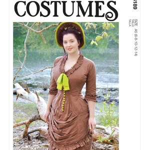 May include: McCall's Costumes pattern M8189 features a woman in a brown dress with a green bow and hat. The dress has a ruffled neckline and sleeves, with a gathered skirt. The pattern includes sizes A5 (6-8-10-12-14).