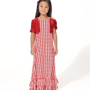 May include: A young girl wearing a red and white heart-patterned dress with a matching red bolero jacket. The dress has a ruffled hem and the jacket has short sleeves. A red hair accessory is visible.