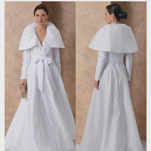 May include: A white, textured formal gown with a matching cape, featuring long sleeves and a bow at the waist. The Vogue Patterns logo is visible in the upper right corner. The pattern number is V2156.